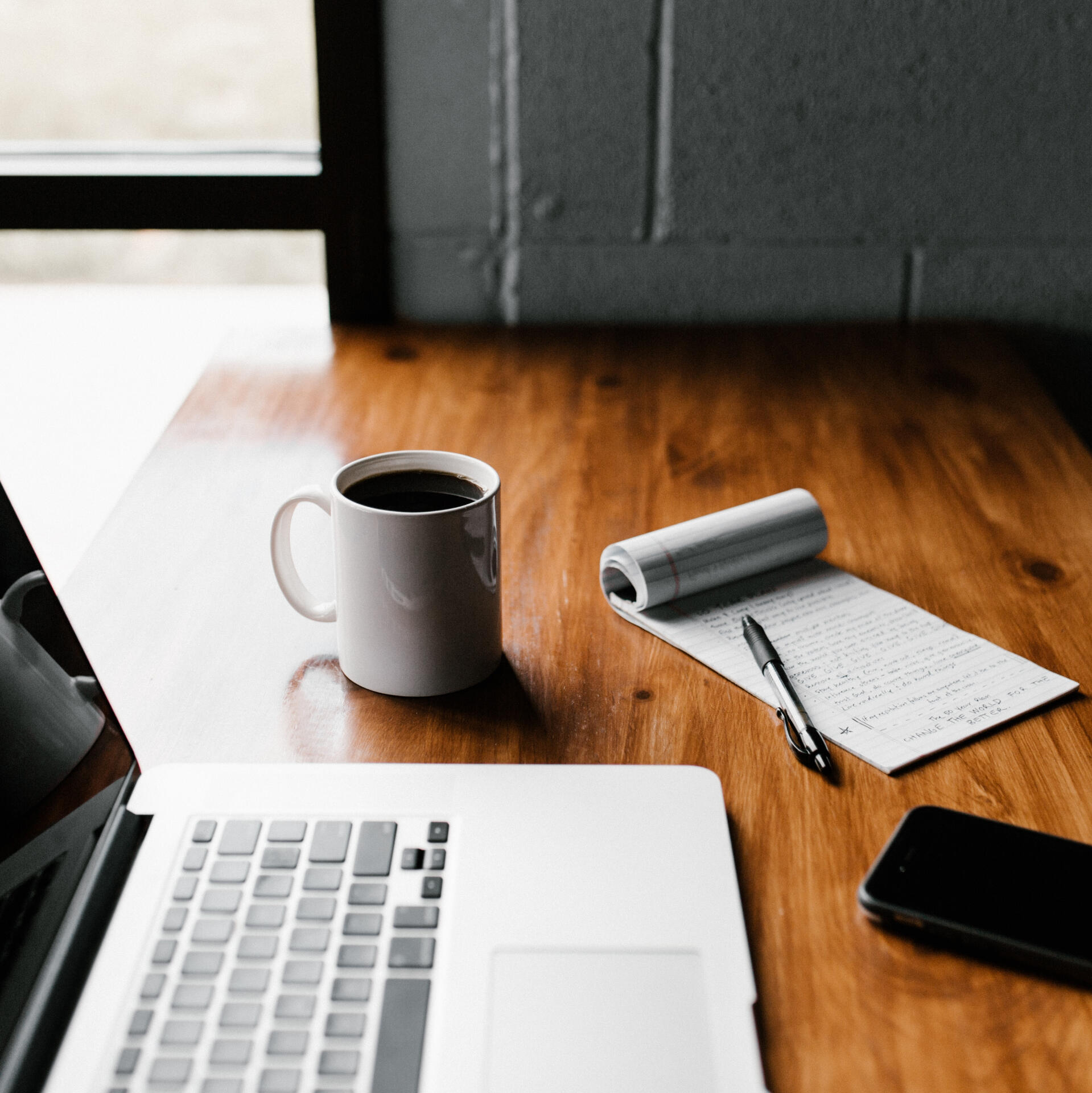 MacBook Pro, white ceramic mug,and black smartphone on table.